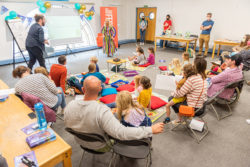 Parents and children inside Bath Central Library. Some are sat on chairs and others on the floor with cushions