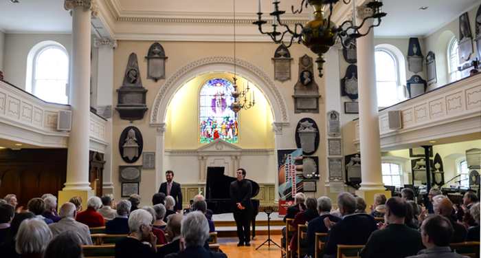 Two gentlemen stood in front of a grand piano in St Swithin's as an audience applauds