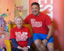 Two volunteers in red Bath Kids Lit Fest t-shirts laughing