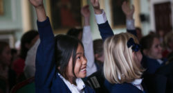 School children with their hands up and smiling