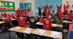 A classroom of children with their hands in the air