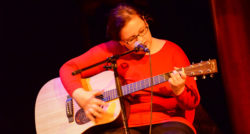 A girl playing the guitar and singing onstage as part of Building Bridges