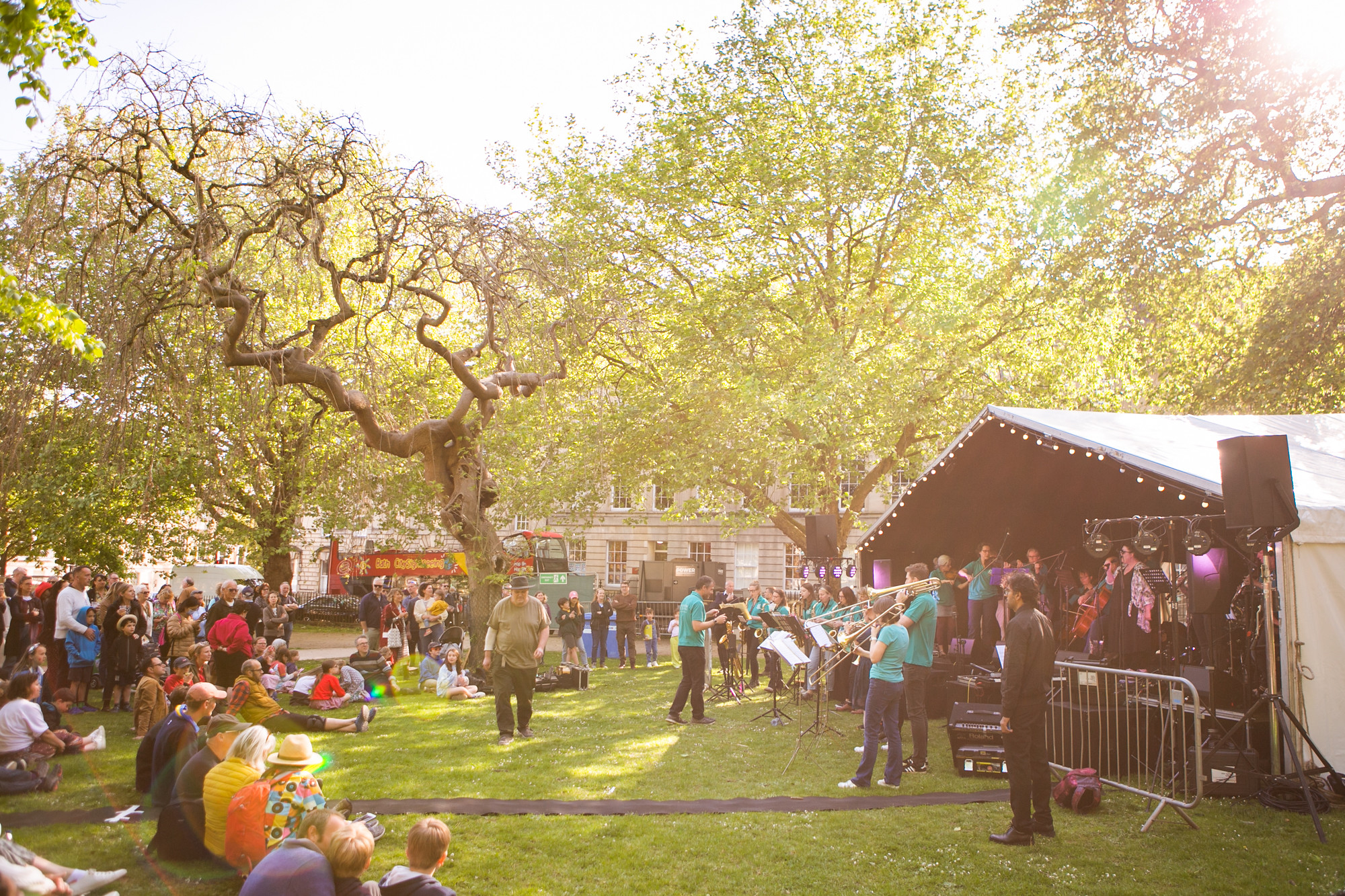 A crowd of people stood and sat on the grass at Queen Square watching a band onstage