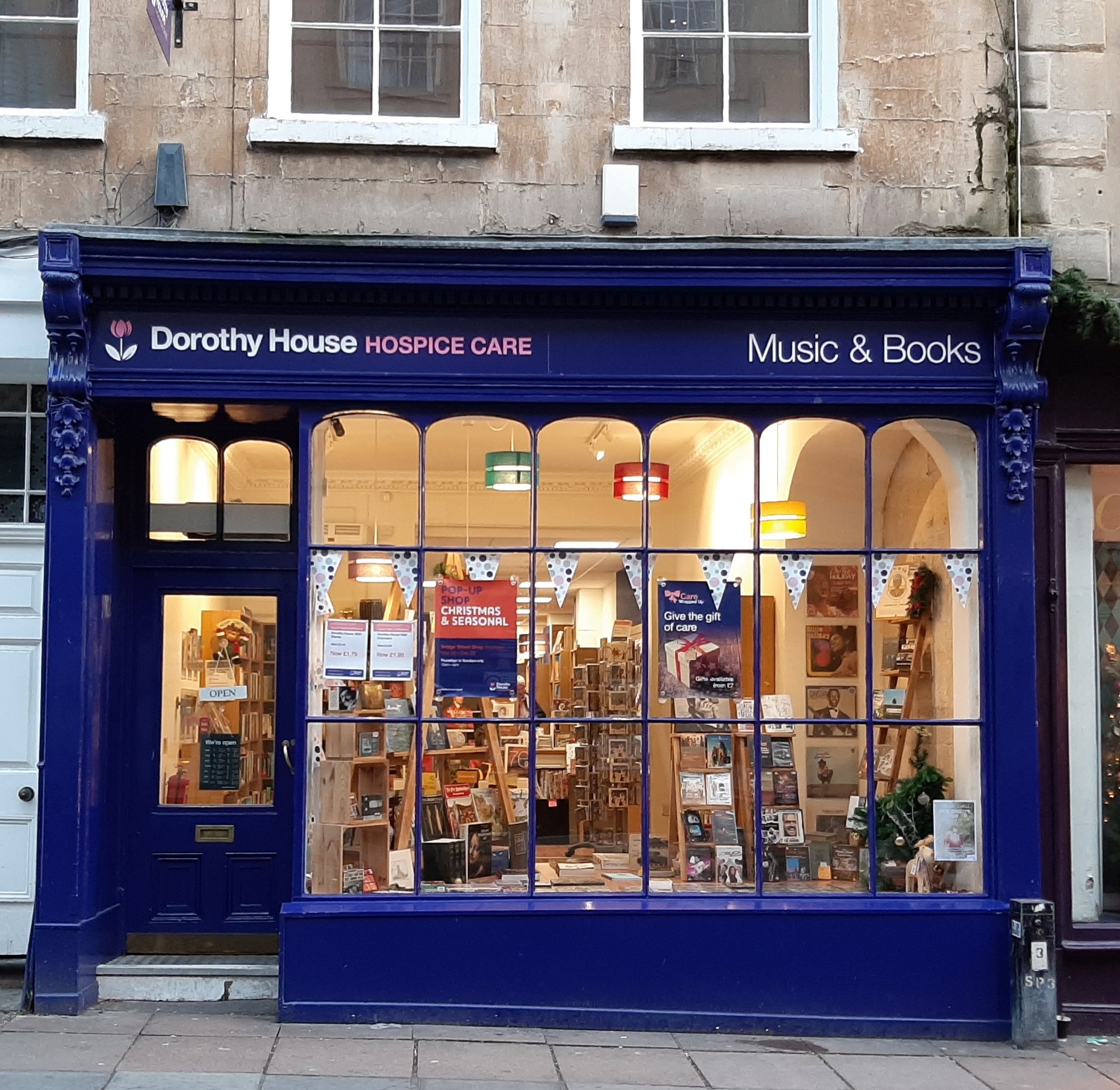 The outside of the shop says 'Dorothy House Hospice Care Music and Books'. There is bunting hanging in the window and lots of books inside