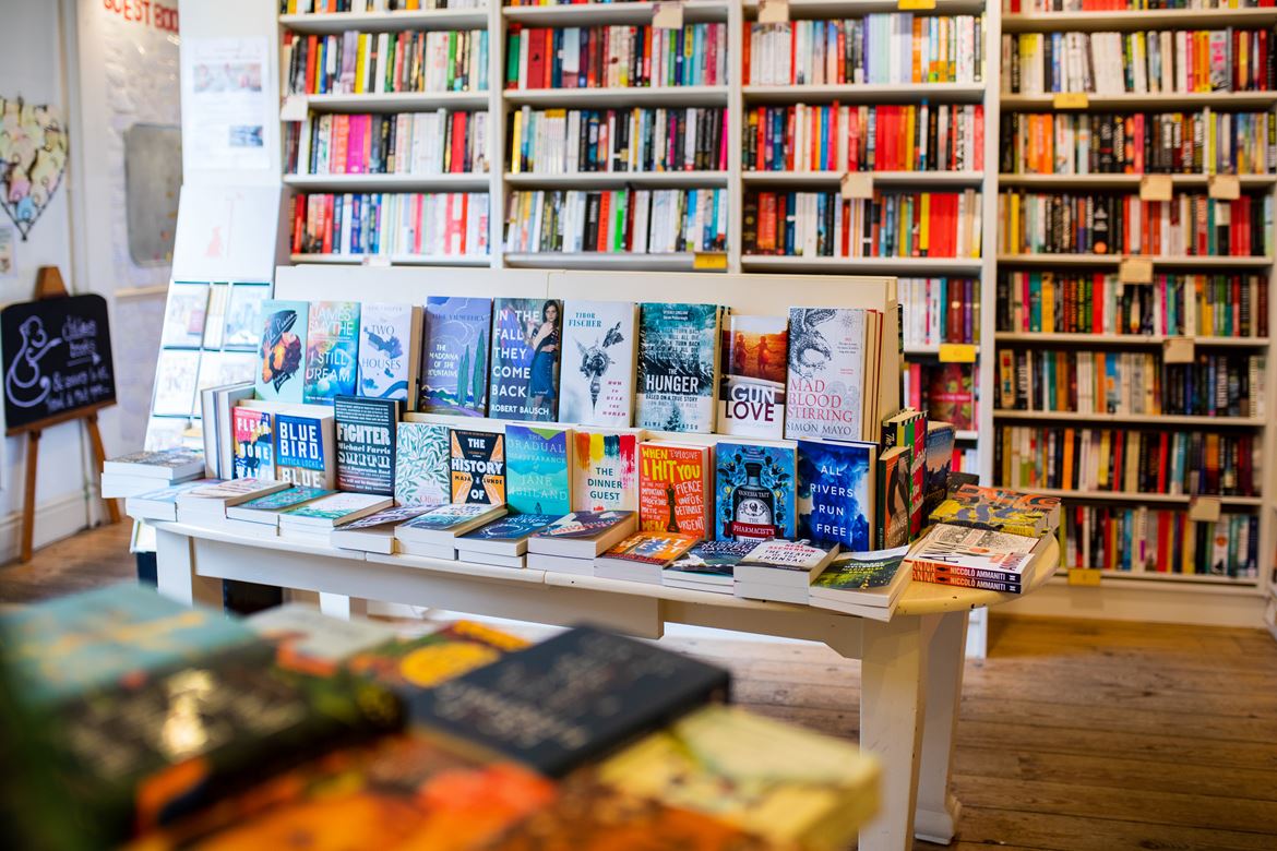 A table of books in front of a wall of bookshelves inside Mr B's Emporium