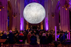 An art installation of the moon inside Bath Abbey. The rest of the Abbey is very dark with multicoloured lights, pulling focus on the moon