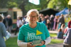A volunteer outside wearing The Bath Festival t-shirt posing for the camera and smiling
