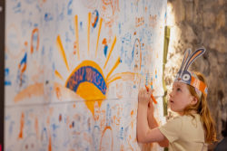 Girl drawing on a mural at the Happiness Hub